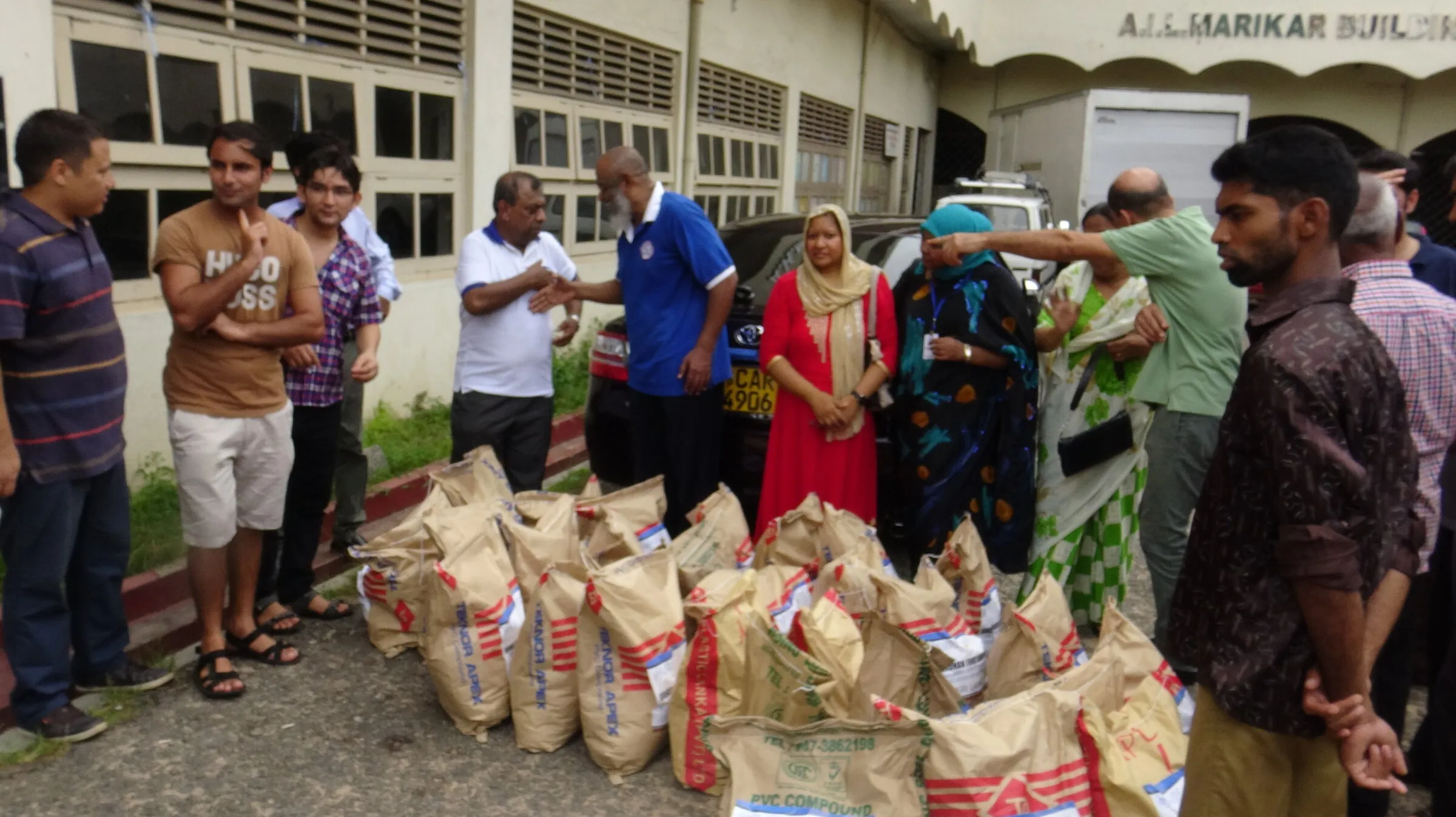 Volunteers and families gather around sacks of food hampers outside a hall.